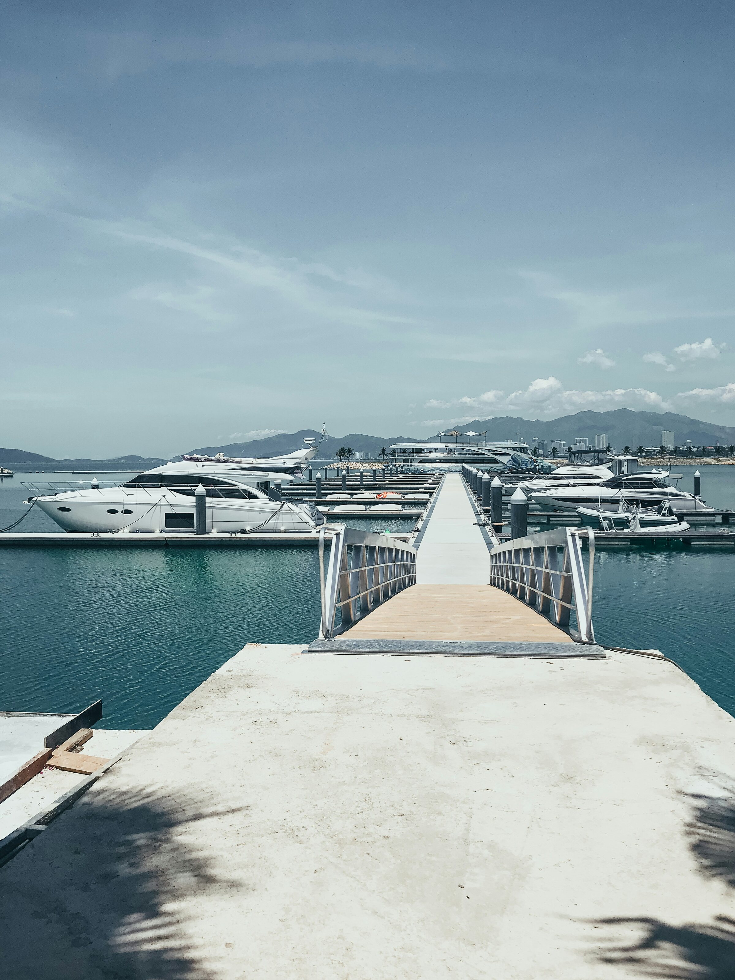 Marina pier leading toward moored yachts with mountains in the distance